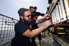 A Navy Engineer inspecting some circuit boards with two people observing