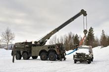 Two Royal Marines in the snow with a crane vehicle hoisting a Land Rover vehicle.