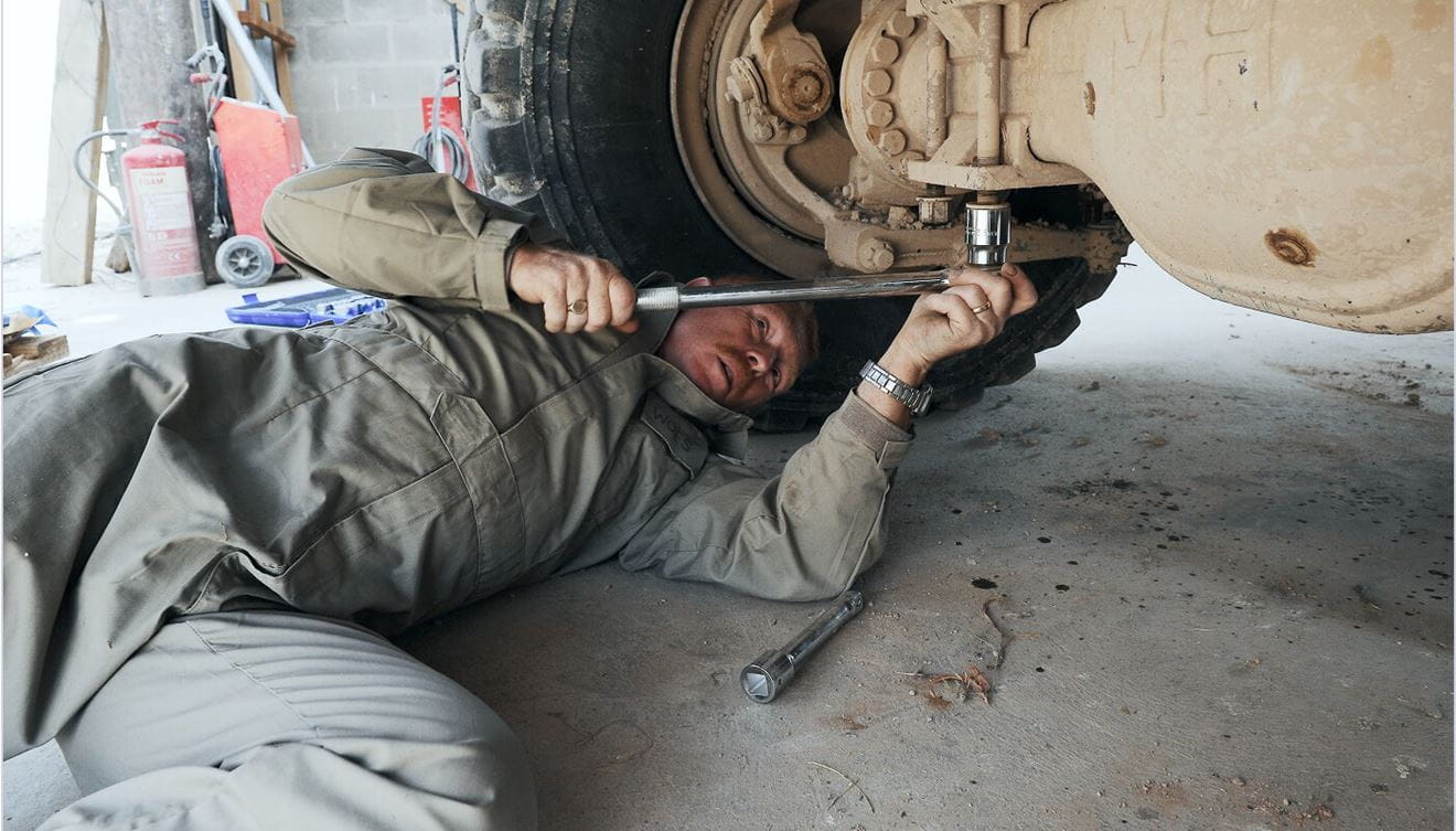 A Royal Marine mechanic laying on the floor with a tool and fixing the underside of a vehicle.