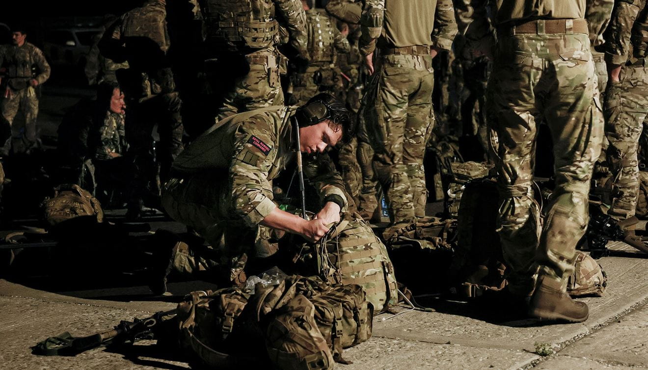 A Royal Marine looking in a bag on the floor.