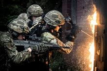 Three Royal Marines with one holding a gun and another one trying to break down a door.