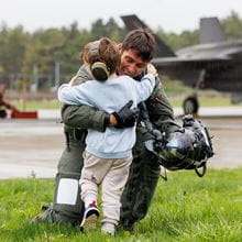 Navy personnel hugging a young child, meeting them off of Carrier Strike Group