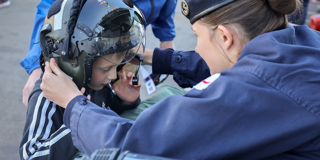 Royal-Navy-Community-02-Our-Local-Community-Centres Female service person with back to camera placing crash helmet on young boy