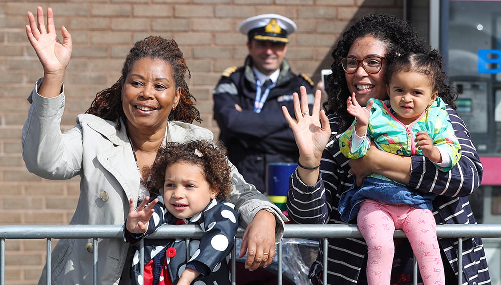 Royal-Navy-Families-07-Community-Centres Two women and children waving with a Navy officer in background