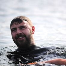 Male swimmer in a wetsuit smiling as he floats on his back in the sea 