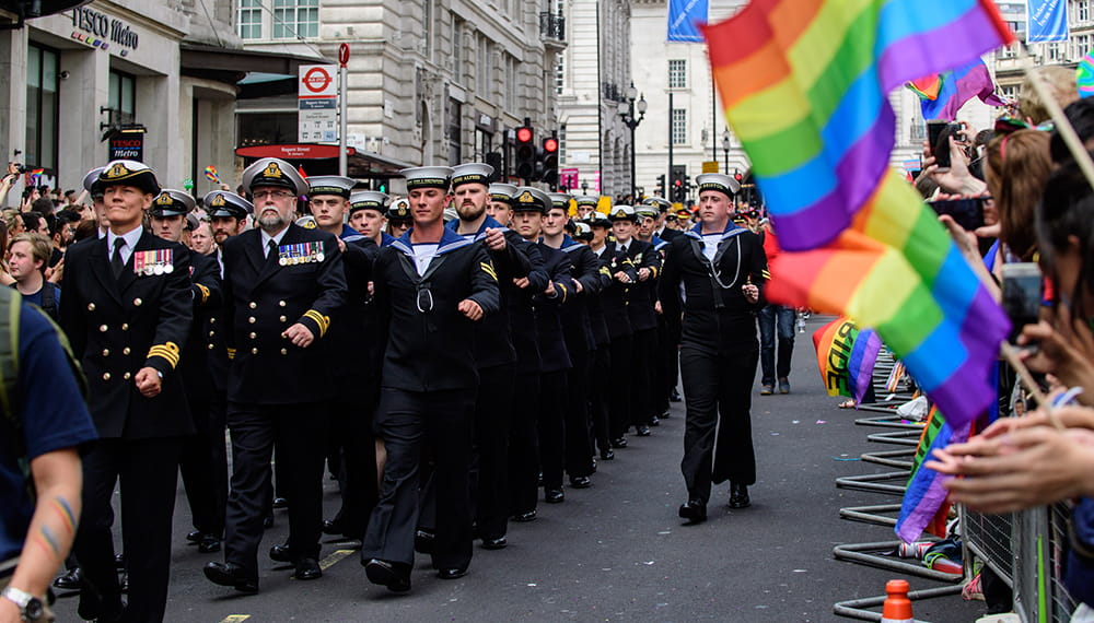 Royal-Navy-Our-People-Ops-for-all-04-lgbtq.jpg Royal Navy sailors march in front of crowd waving Rainbow flags