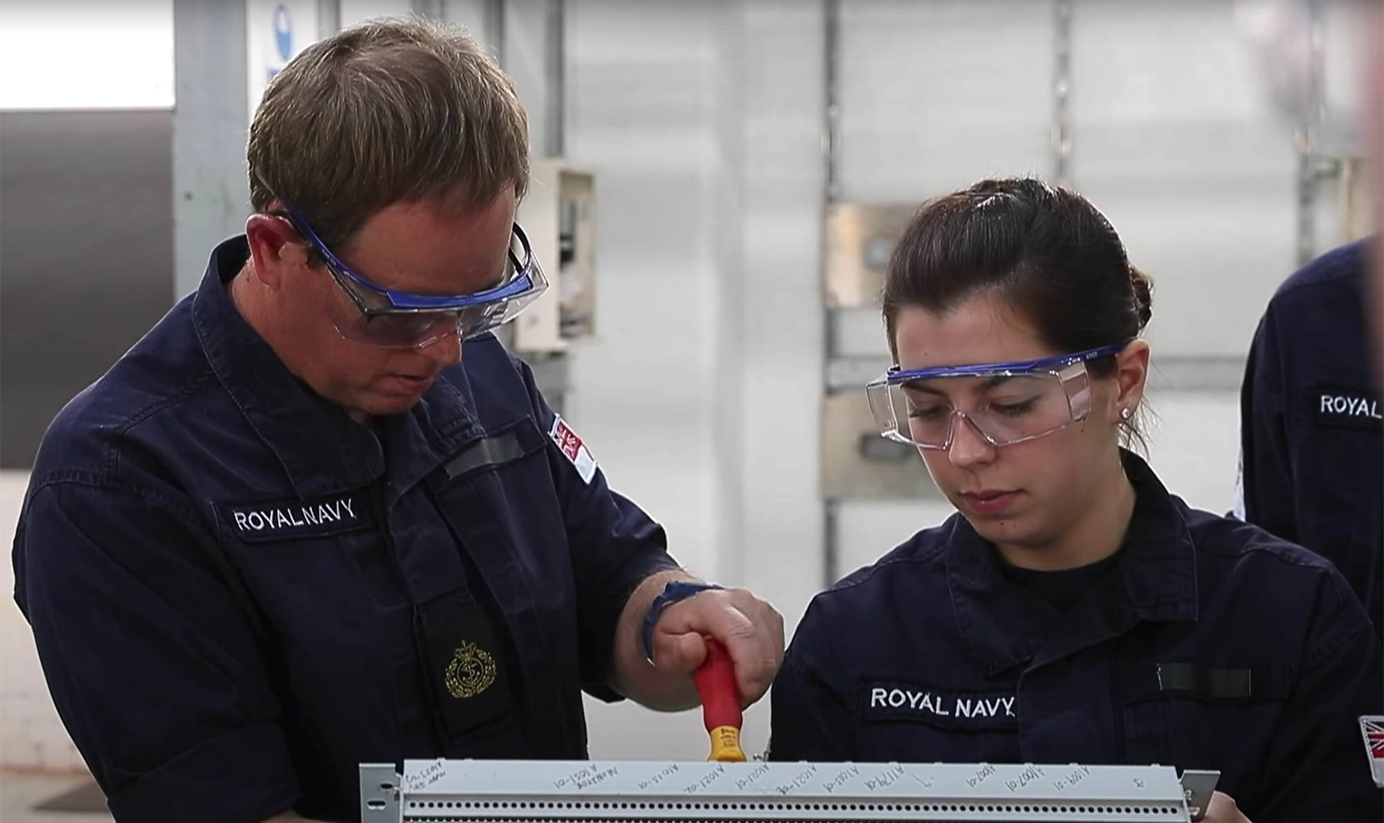 Two Royal Navy Personnel working wearing protective glasses.