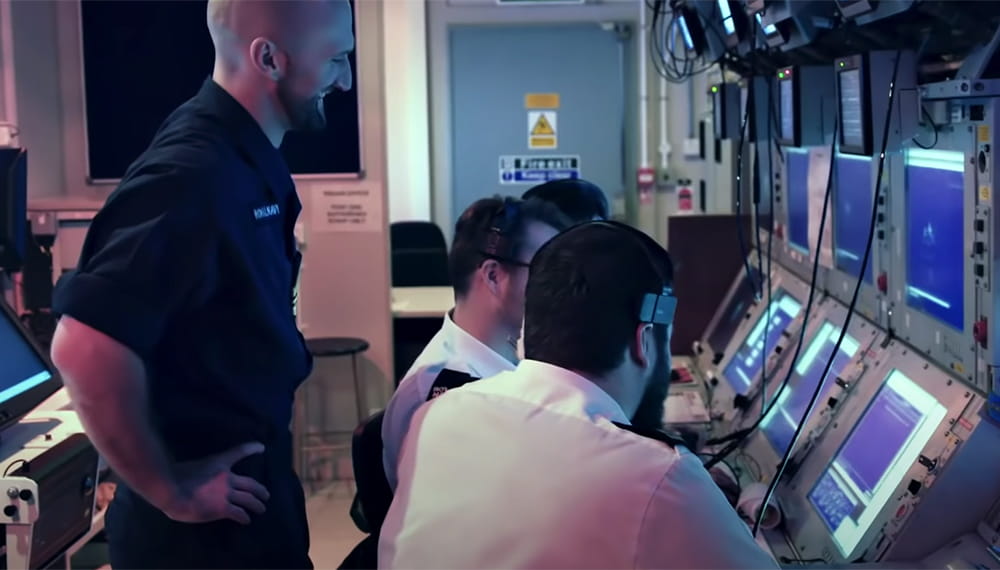 blue uniformed crewmember looks on as white shirted colleagues explain data shown on computer screens