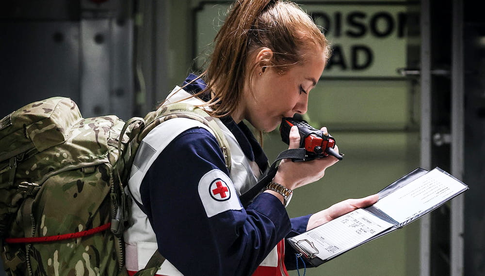 Healthcare personnel talking into a radio reading from a document with a backpack on