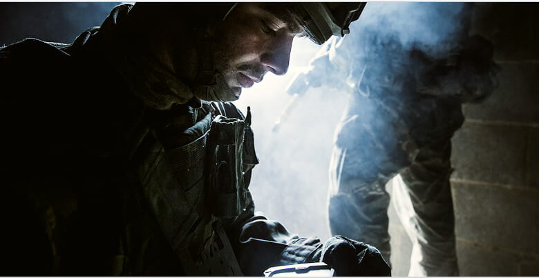 A Royal Marine in the foreground looking at screen and in the background are the legs of a Royal Marines.