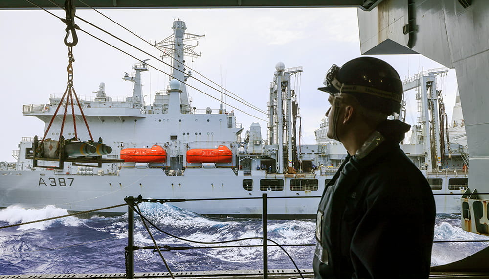 Personnel looking at the HMS Queen Elizabeth while deployed with the UK carrier strike group, completing a transfer of live munitions.