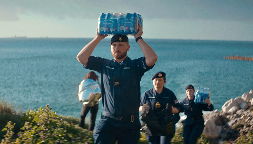 The image shows three navy personnel carrying supplies near the sea. The surface fleet defends the UK’s interests, keeps global trade flowing and provides support to civilians affected by natural disaster.