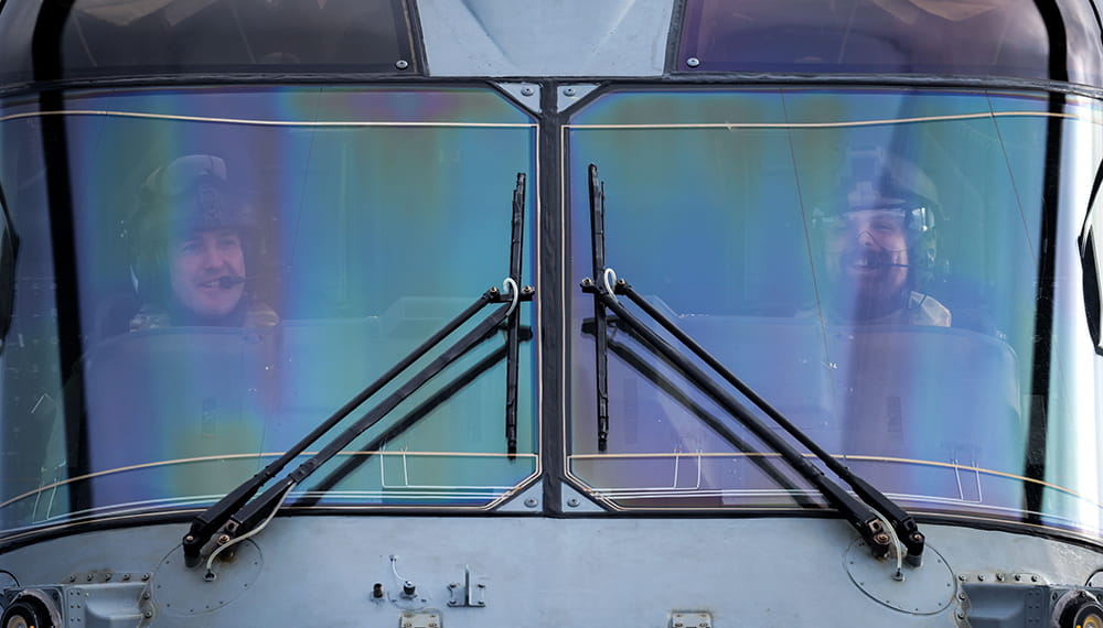 Lieutenant commander and co pilot pictured head on in merlin Mk2 helicopter cockpit with reflections of sky on cockpit screen