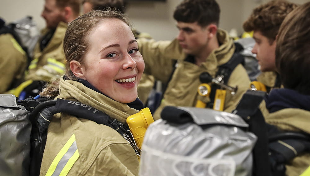 A group of people wearing fire fighter gear. One looks back at the camera smiling.