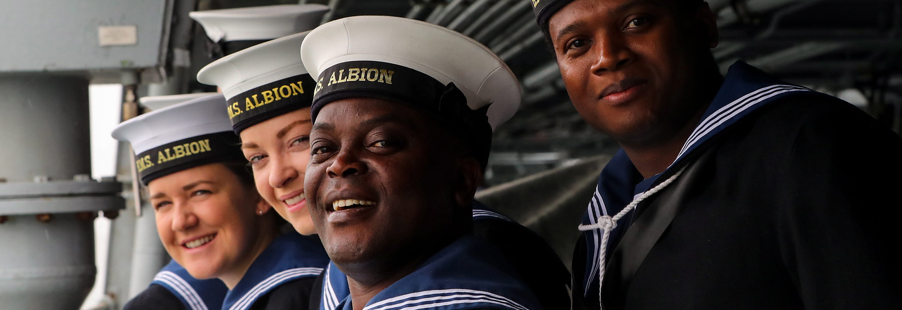 A group of Royal Navy sailors in their number 1 uniform smiles at the camera