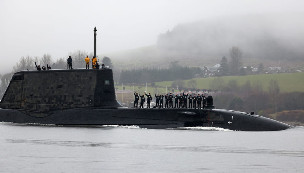 A group of submariners stand on a submarine that has ascended in the port of Clyde
