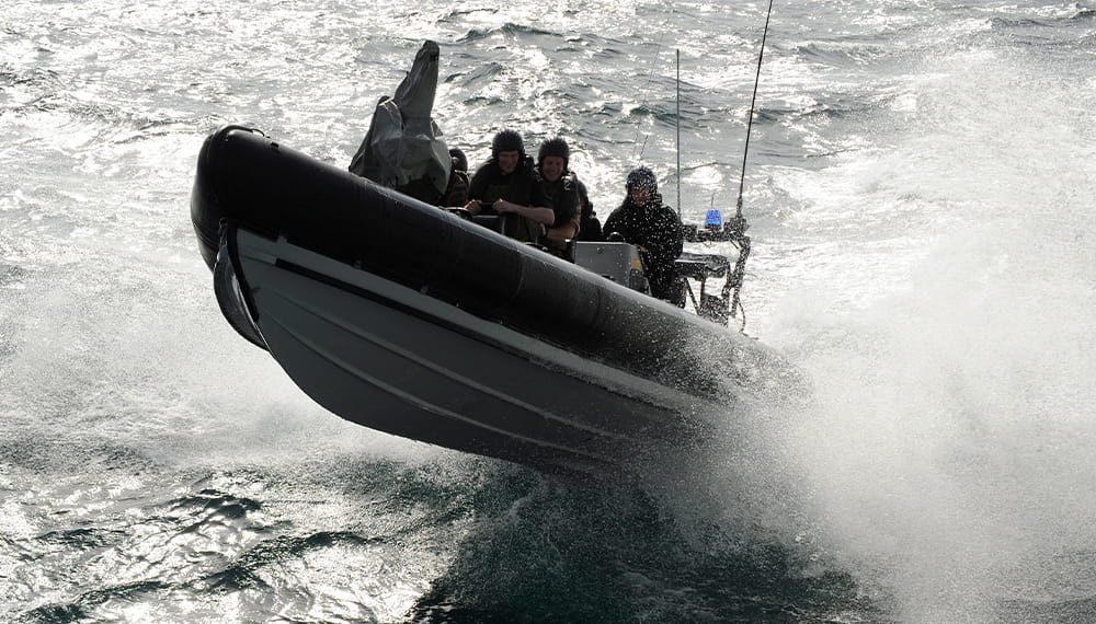A black rib boat with its front side mid-air approaches the camera in the sea