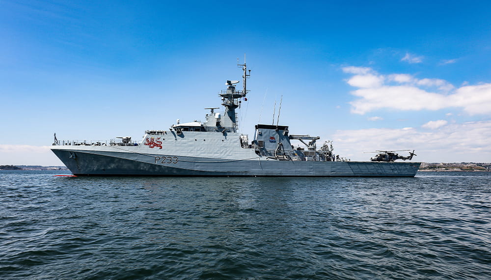 HMS Tamar, a River class ship, sails on a blue-sky day and calm waters