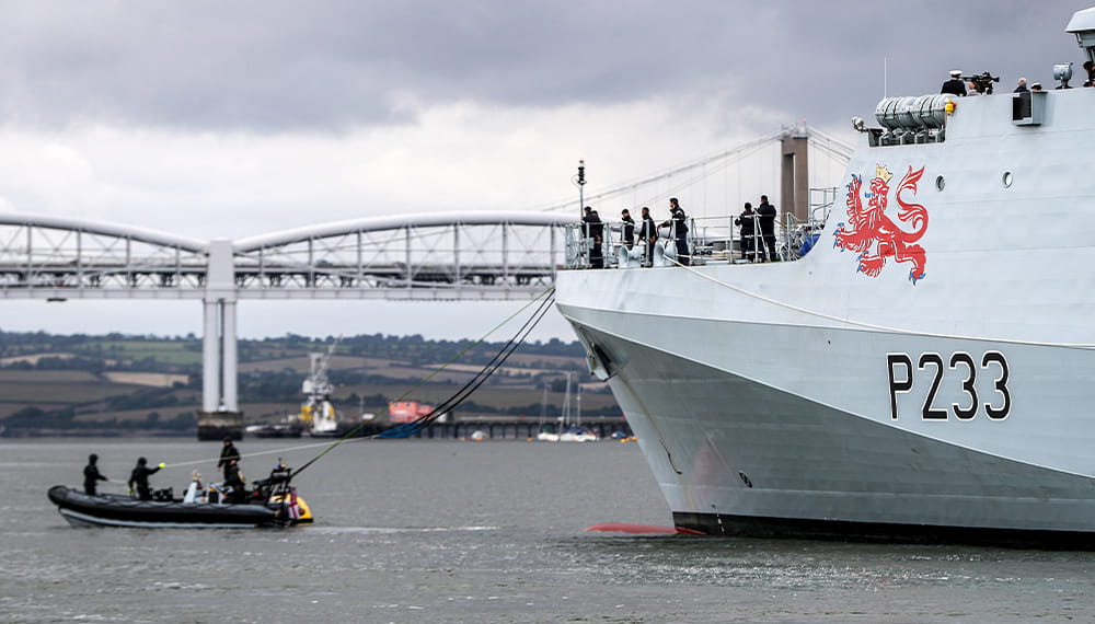 A small black rib boat  giving personnel aboard the HMS Tamar rope to connect the two boats