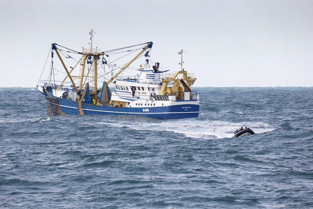 A fishing vessel out at sea with a rib boat approaching the camera in the distance