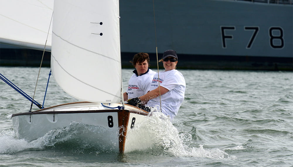 2 sailors in a small white boat sail towards the camera
