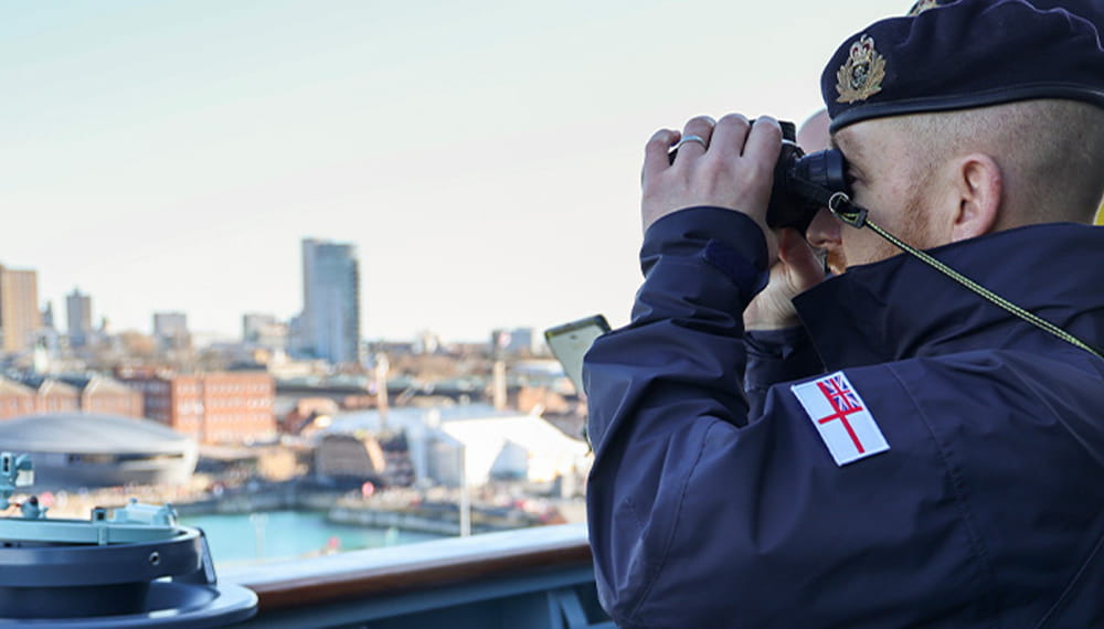 Navy sailor looks through binoculars at the port