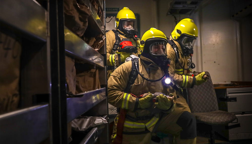 3 sailors in fire protective gear searching through a boat