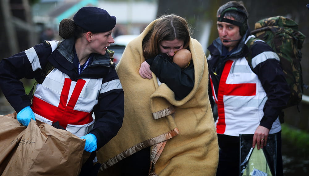 Two Royal Navy medics support lady and a baby wrapped in a blanket